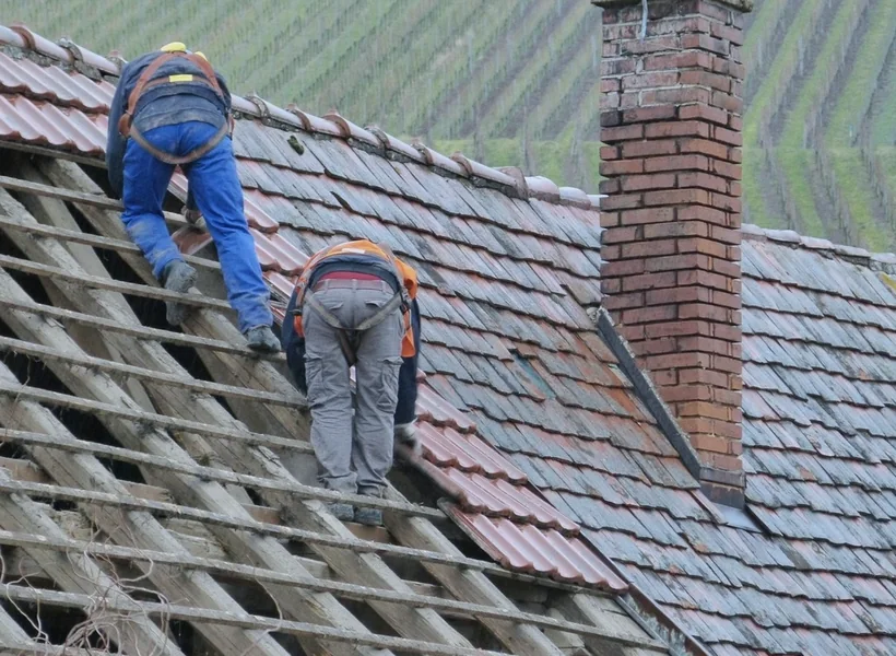 Zwei Dachdecker entfernen alte Ziegel von einem Steildach